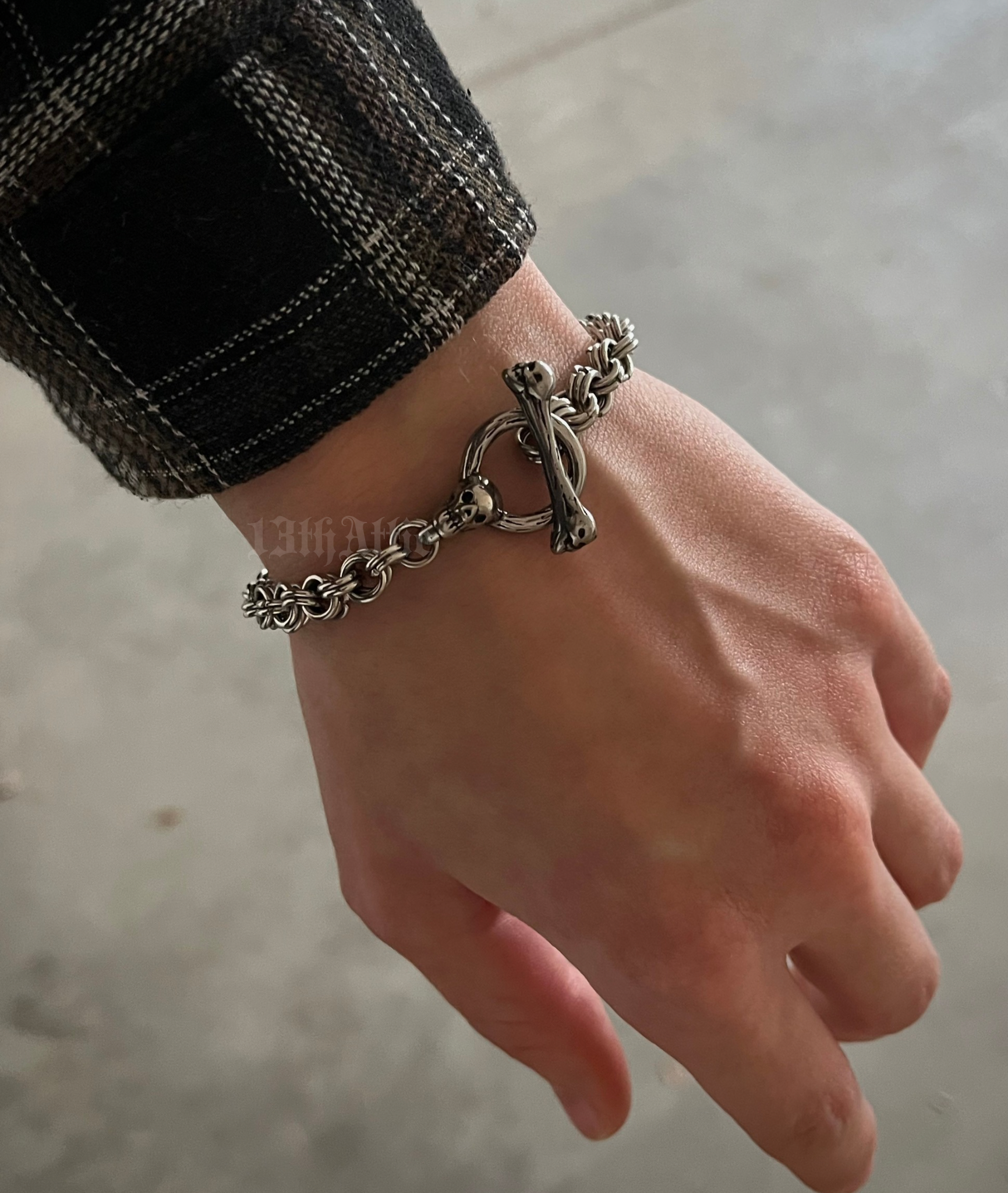 Hand of a person wearing a handmade stainless steel chainmaille bracelet with a skull clasp, featuring an intricate weave and polished finish. A bold, edgy accessory perfect for gothic, biker, and alternative fashion.